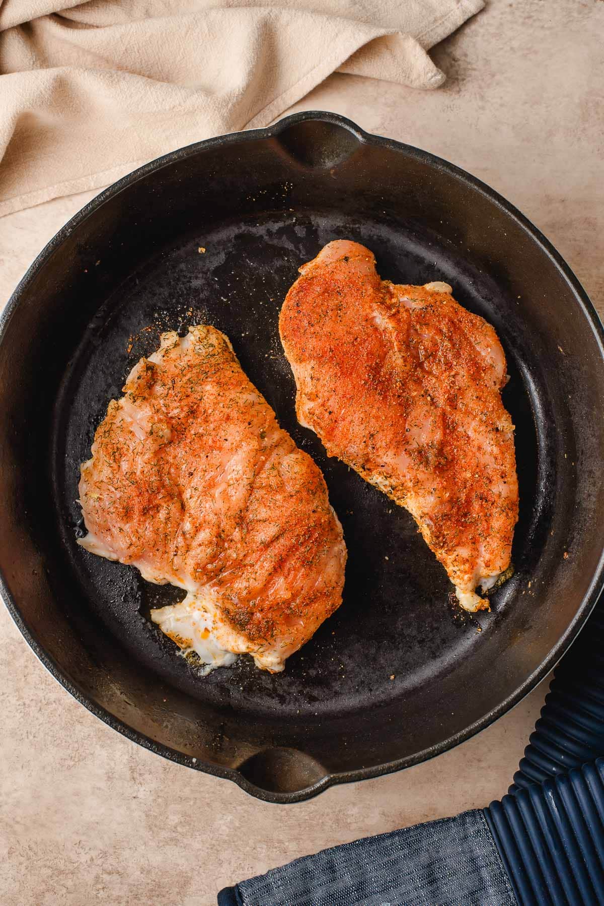 Two chicken breasts in a large cast iron skillet.