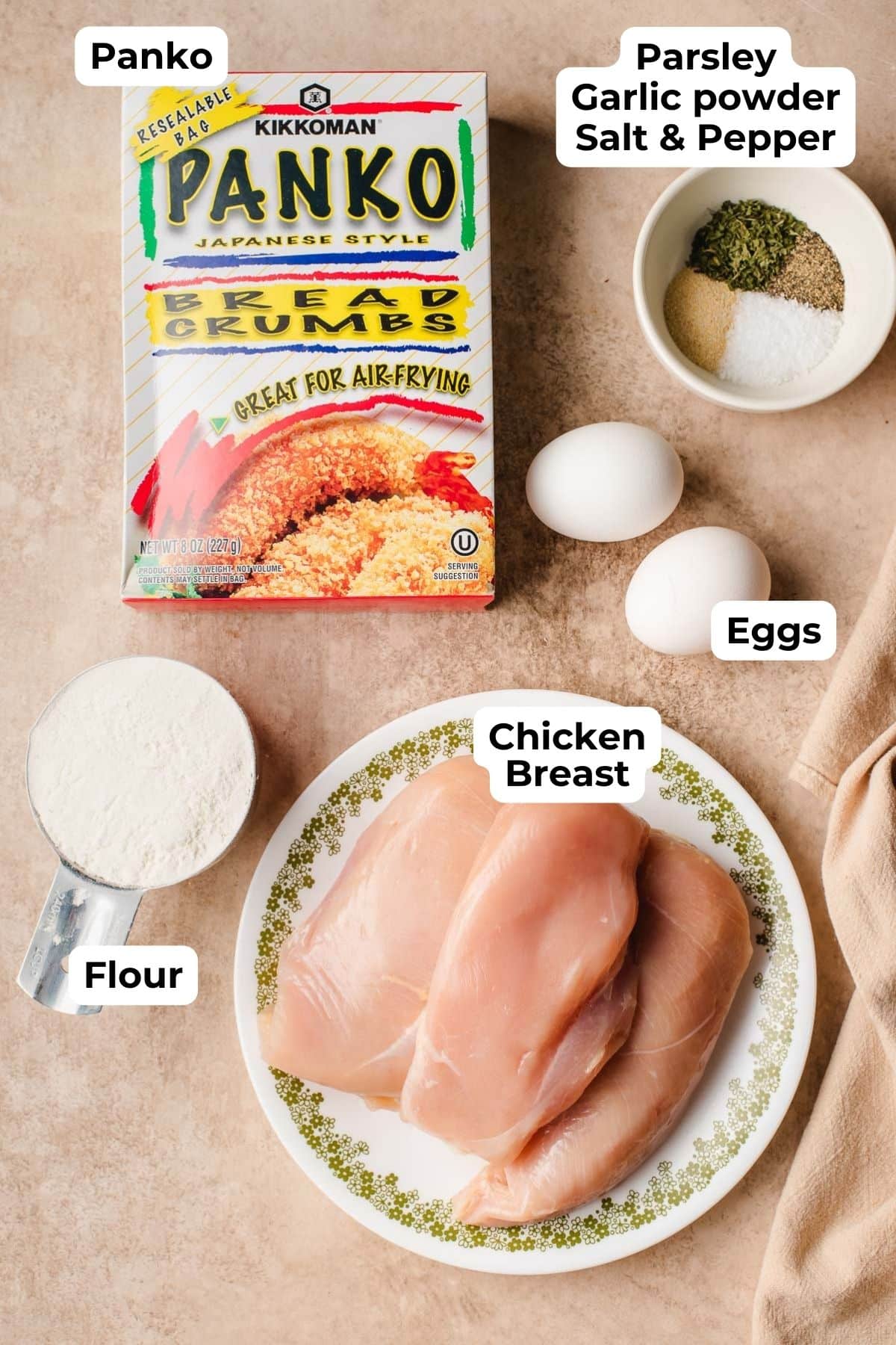 recipe ingredients for crispy chicken cutlets on a counter including raw chicken, panko, eggs, flour, and seasonings