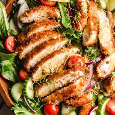 a crispy chicken salad with a sliced chicken cutlet on top.