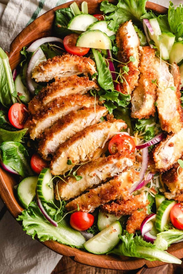 a crispy chicken salad with a sliced chicken cutlet on top.