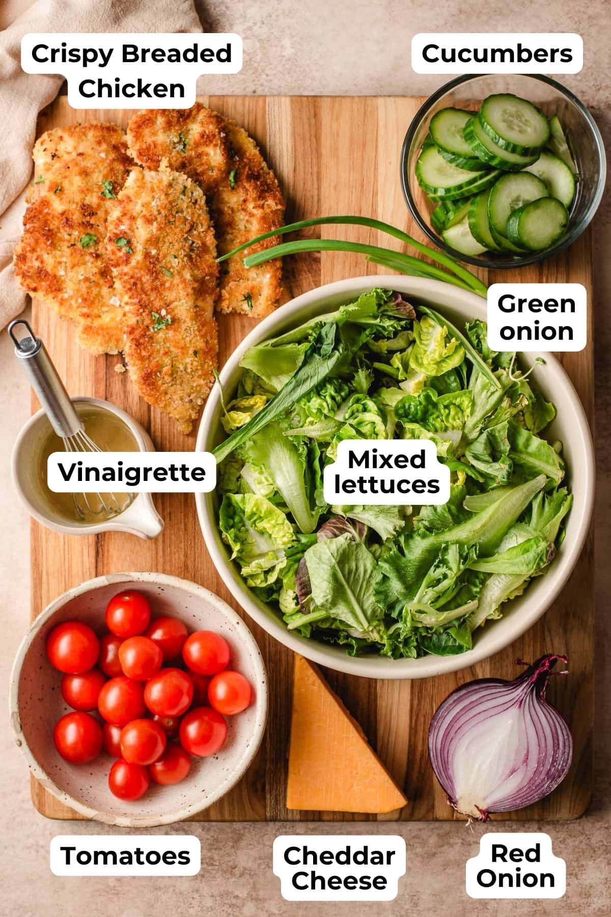 ingredients for a crispy chicken salad including lettuce, crispy chicken cutlets, tomatoes, cucumbers, cheese, onions, and dressing