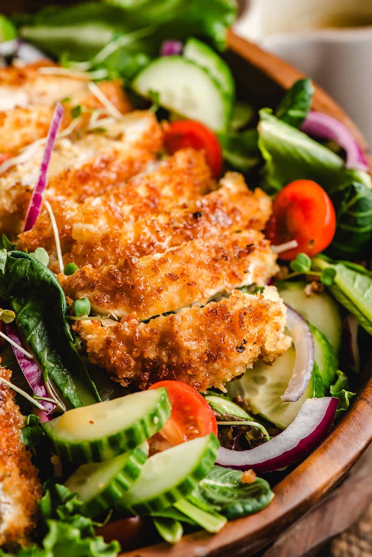 a chicken cutlet sliced atop on a salad with mixed greens and veggies