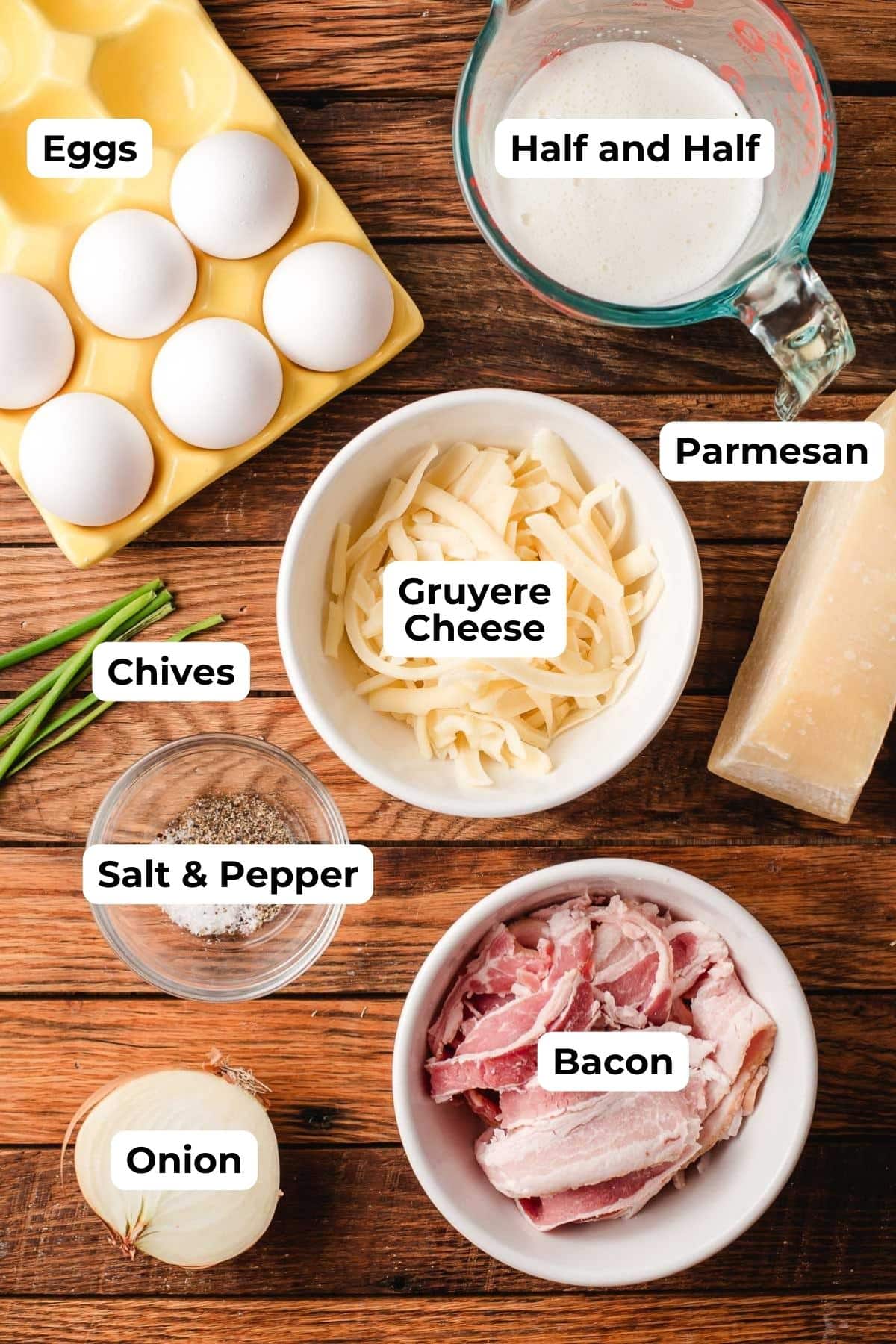 Eggs, half and half, cheeses, chives, seasoning, and bacon on a wood background.