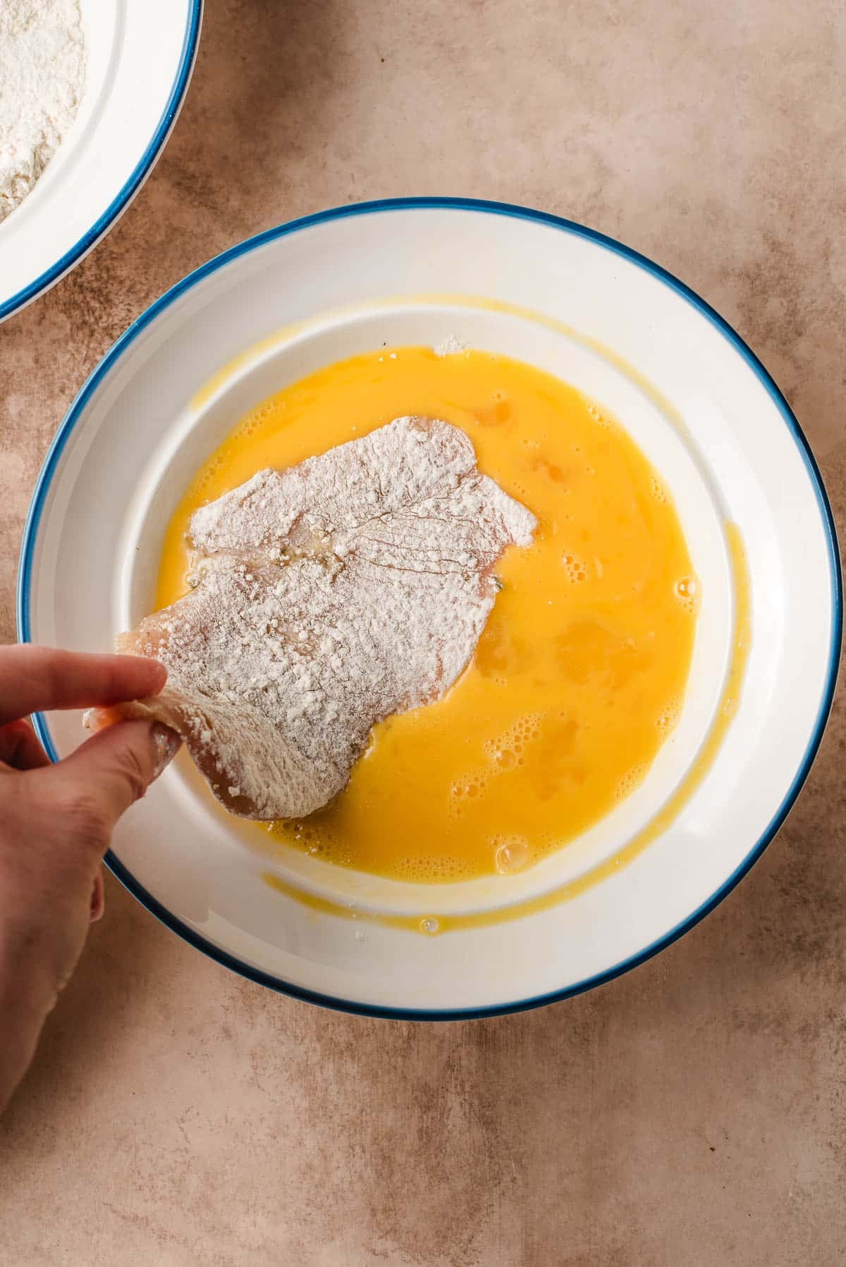 dipping a floured piece of chicken into the egg mixture