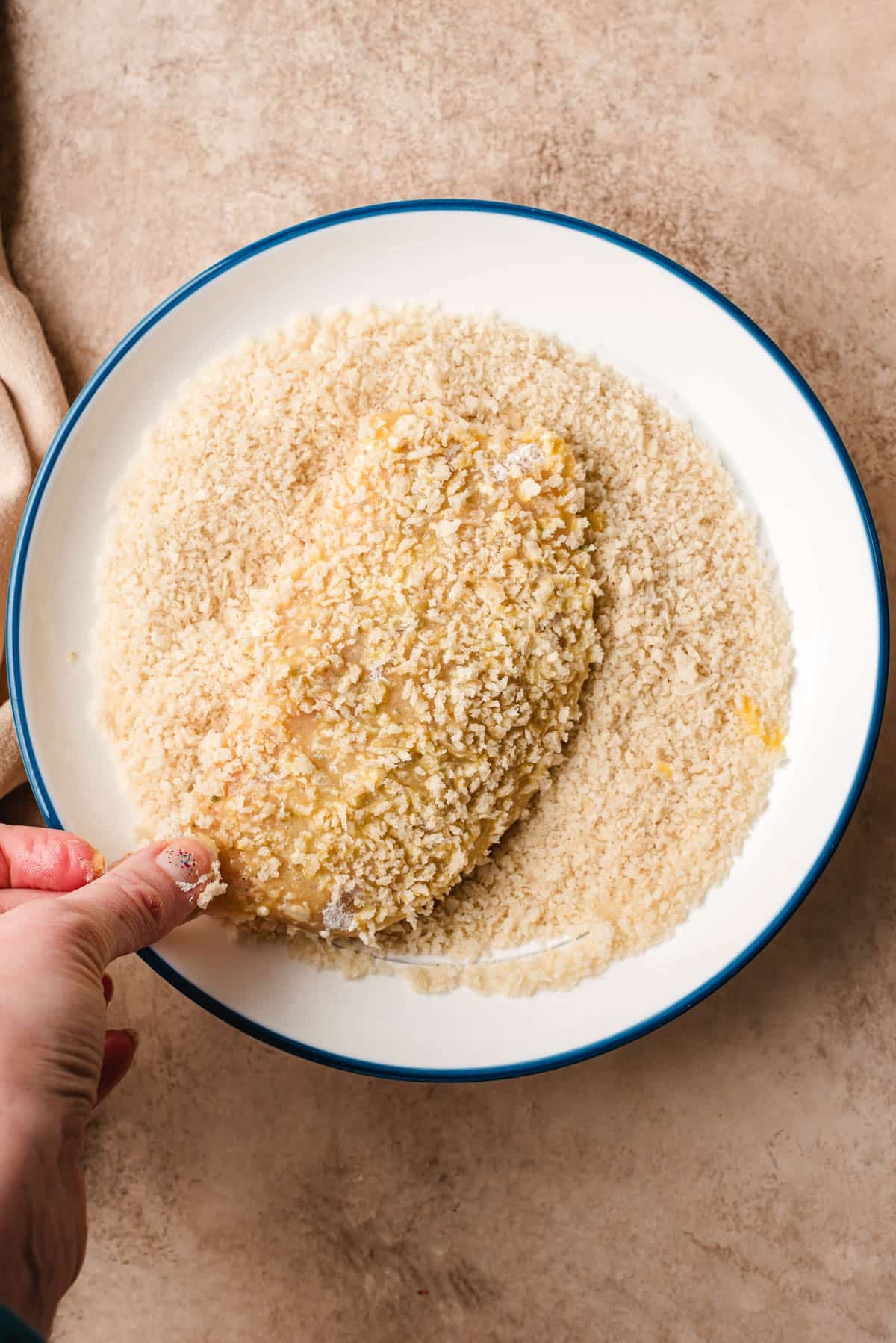after dredging the chicken in flour and egg, the chicken is being dipped into panko