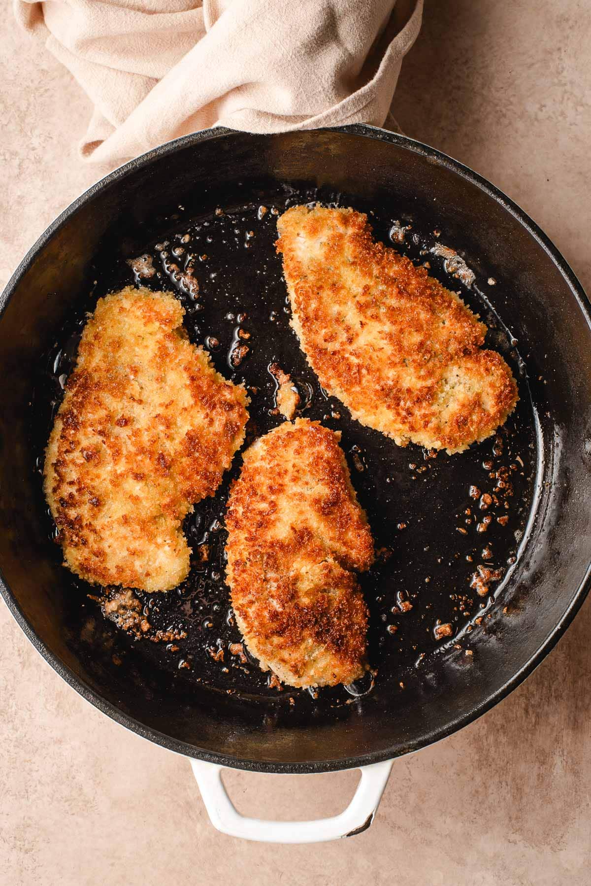 chicken cutlets frying in a cast iron pan
