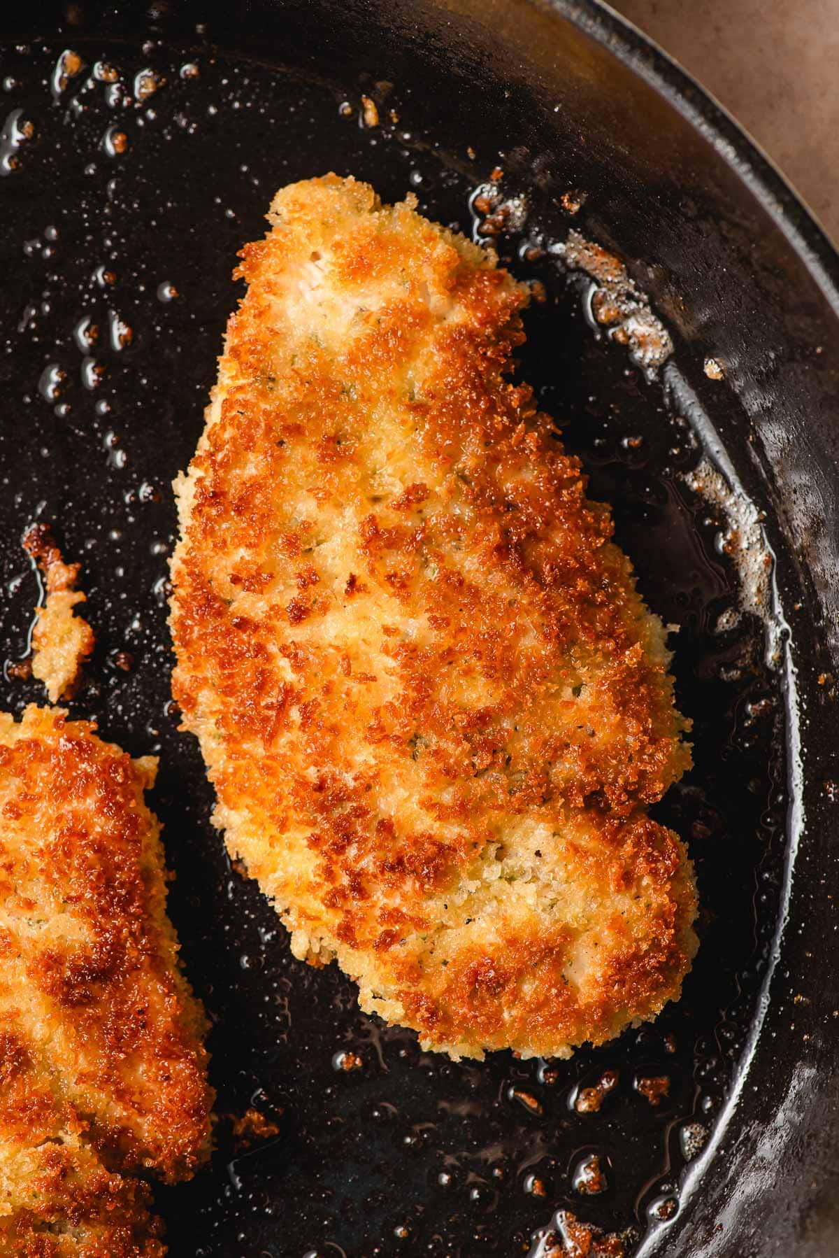 a close up shot of a piece of chicken frying in a cast iron pan