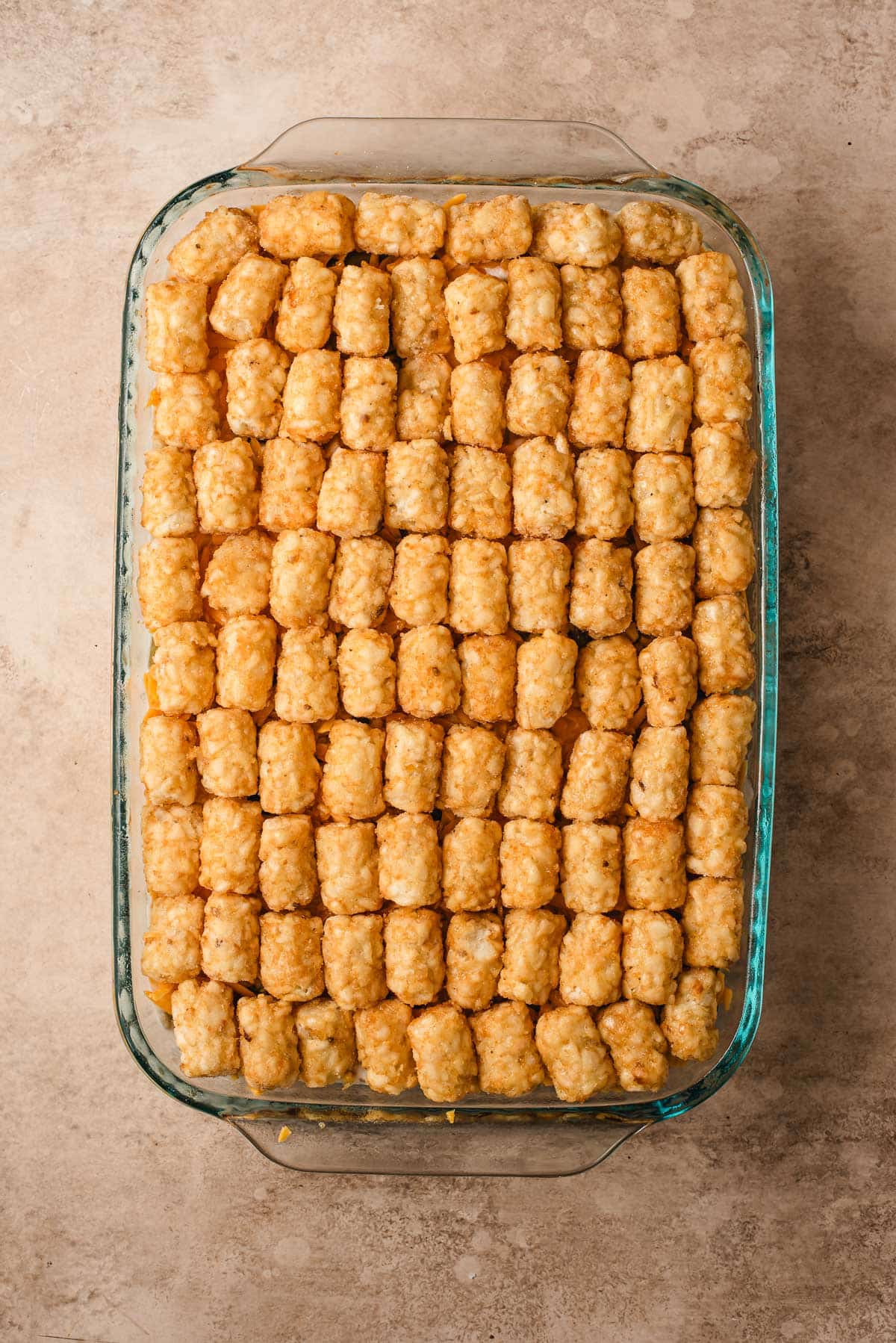 arranging the tater tots atop the green beans, ground beef, and cheese