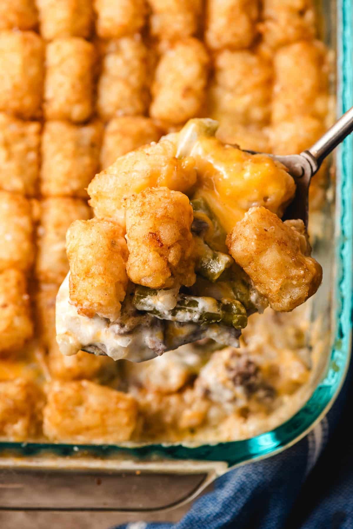 a spoon scooping a portion of tater tot casserole out of a casserole dish