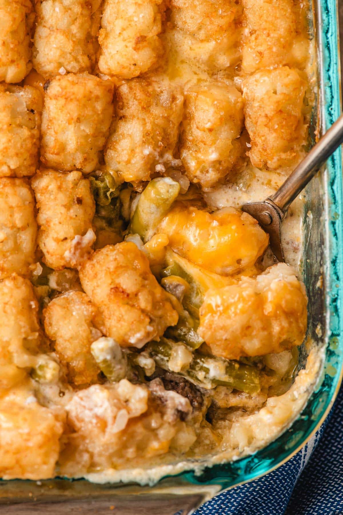 an up close photo of green bean tater tot casserole getting scooped out of a casserole dish