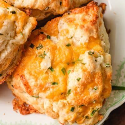 Overhead shot of a cheddar chive scone on a plate with melty cheese on top.