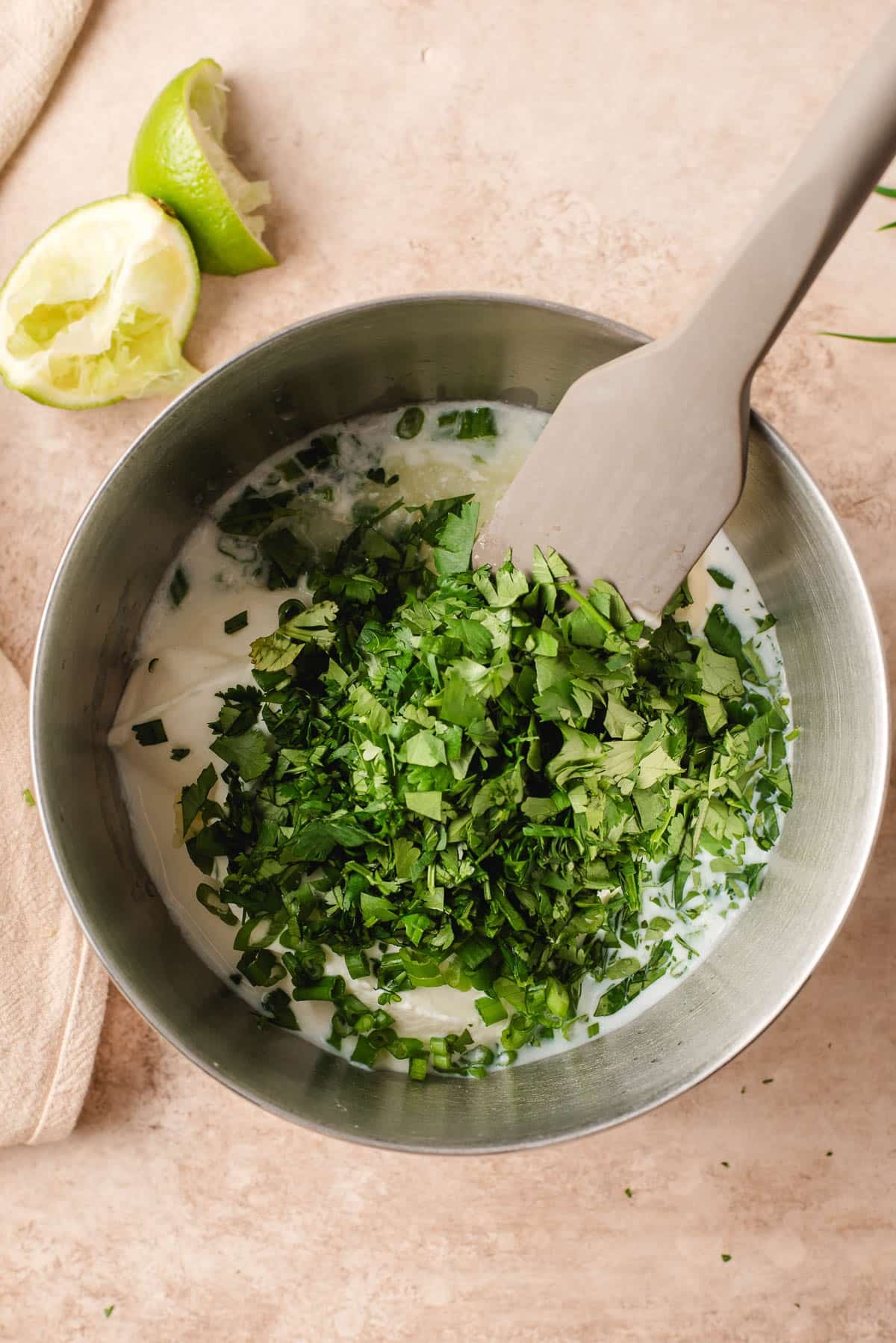 Cilantro and chives stirred into mayo and sour cream in a metal mixing bowl.