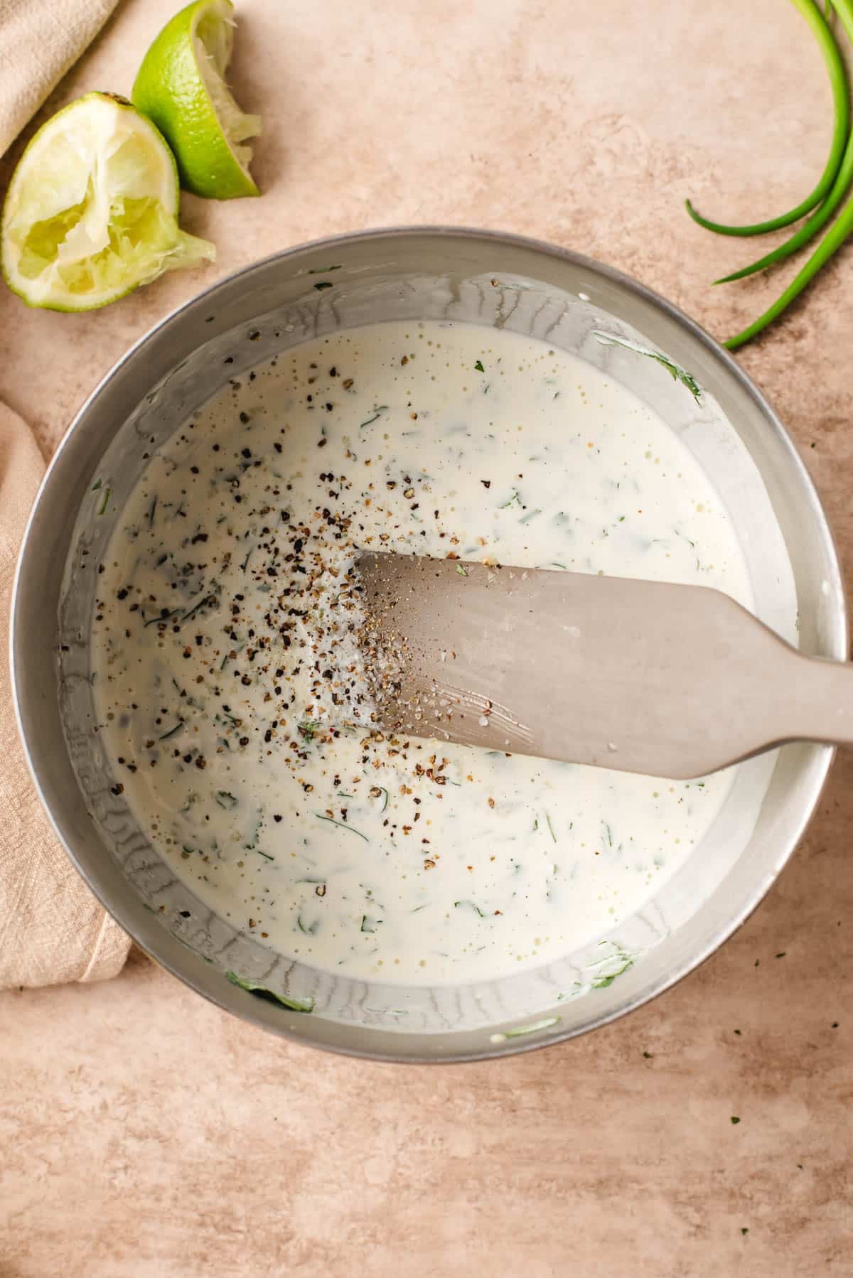 Mayo, sour cream, lime, cilantro, garlic, salt, and pepper being stirred in a metal bowl.