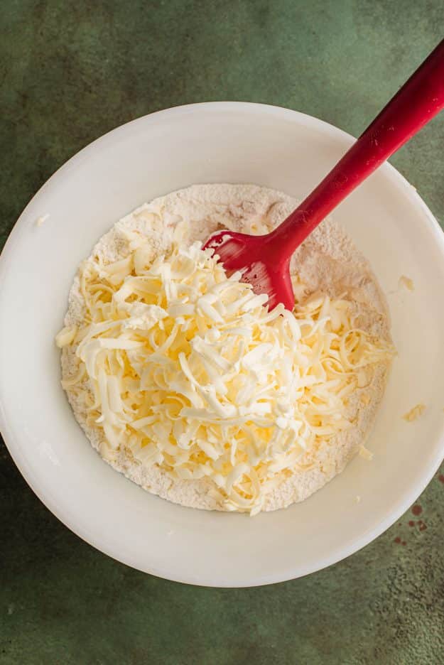 Folding cold grated butter into dry ingredients in a bowl.
