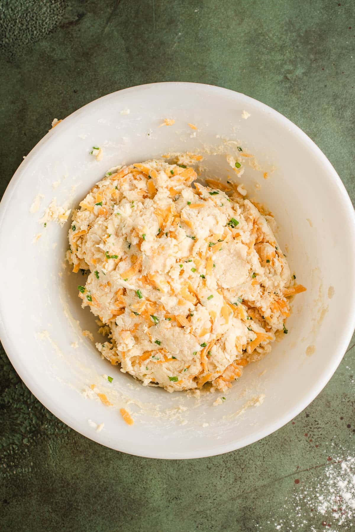 Cheddar cheese and chives added to the scone dough in a bowl.