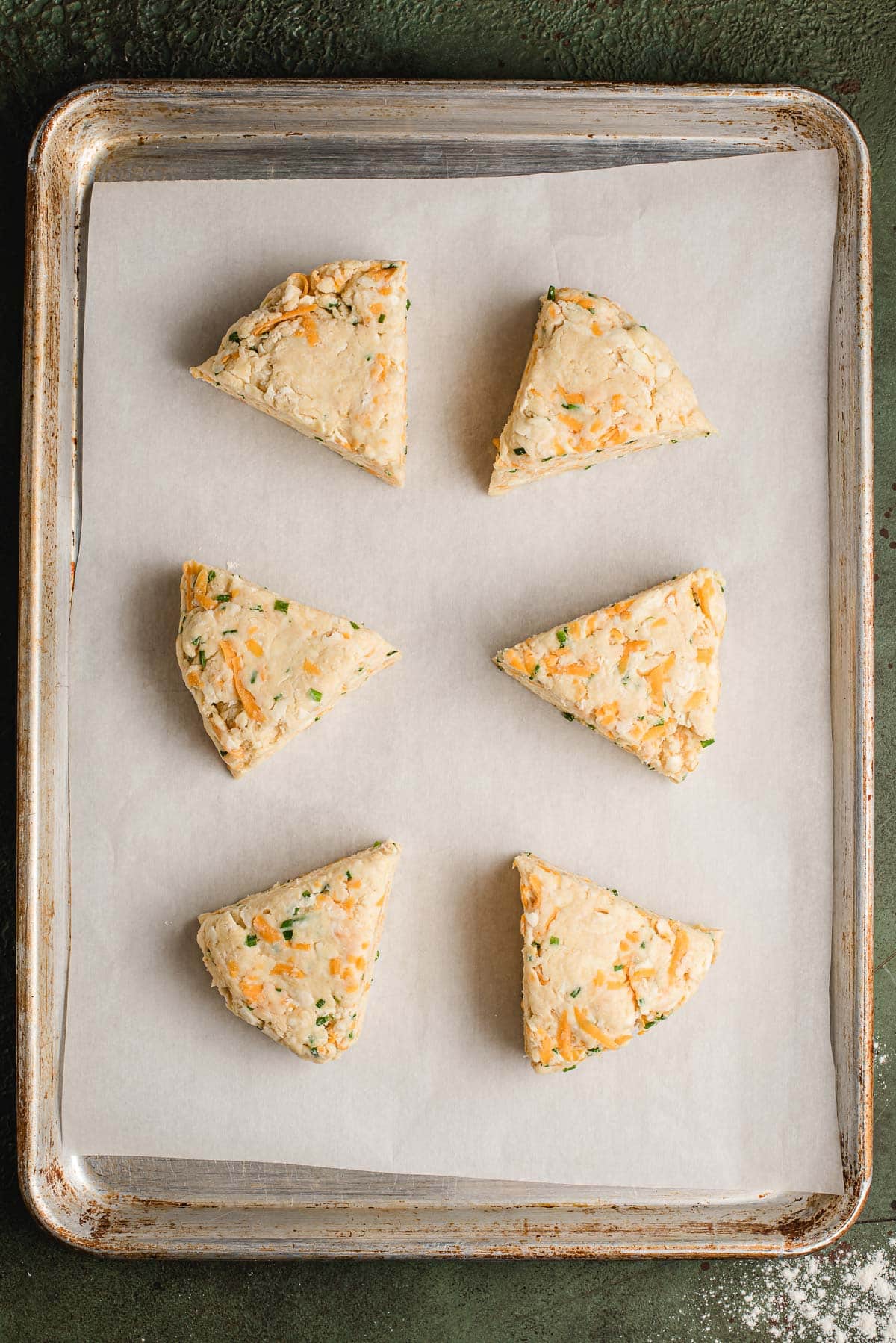 Six cheddar chive scones on a sheet pan before baking.